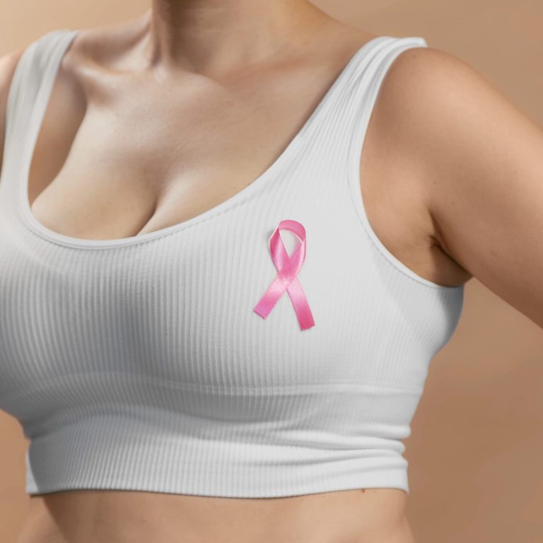 Young lady in a white top with a ribbon sign on her chest to support pink October and females combating breast cancer. Anonymous studio shot photo on beige background.